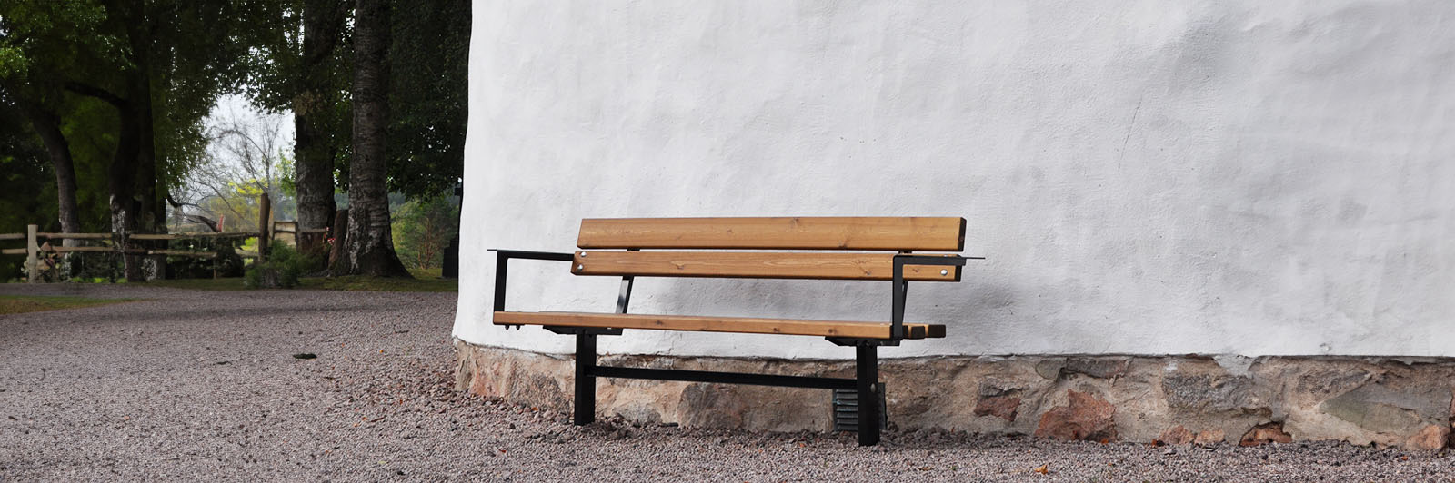 A park bench with armrest against a wall of a building.